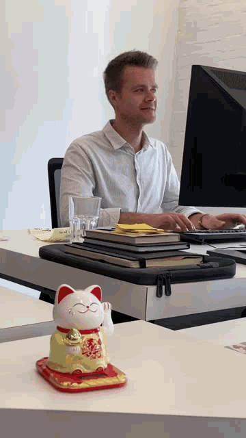 a man sits at a desk with a lucky cat figurine