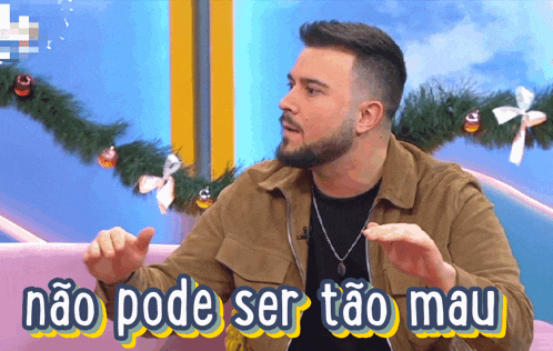 a man with a beard is sitting in front of a sign that says não pode ser tao mau