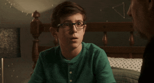 a young boy wearing glasses and a green shirt is making a face