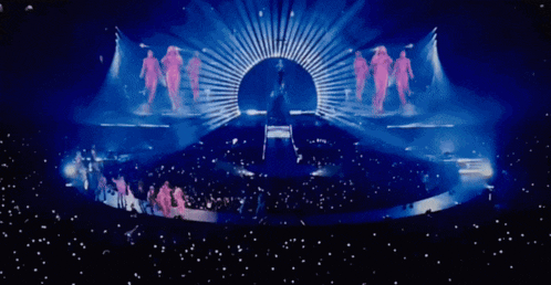 a group of people are dancing on a stage in front of a large screen