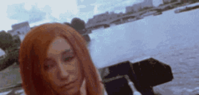 a woman with long red hair is standing in front of a river .