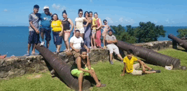 a group of people posing for a picture with cannons in the foreground and the ocean in the background