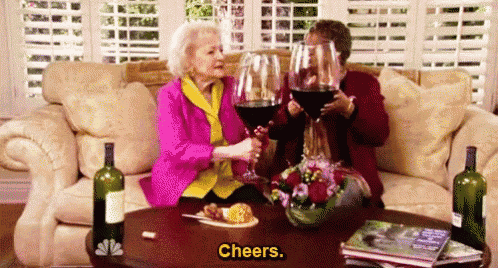 two older women are sitting on a couch holding glasses of red wine .