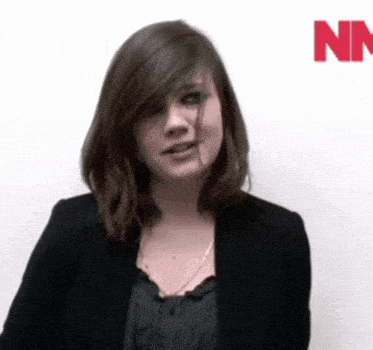 a woman in a black jacket is standing in front of a white wall with the letter n on it