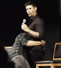 a man is holding another man in his arms while standing in front of a microphone .