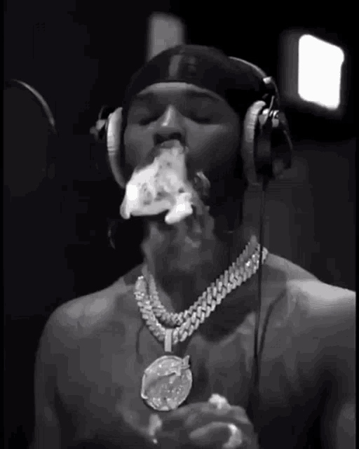 a man wearing headphones and a necklace is smoking a cigarette in a black and white photo .