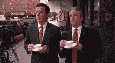 two men in suits and ties are holding cups of coffee on a city street .