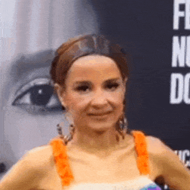 a woman in an orange top and earrings is standing in front of a black wall .