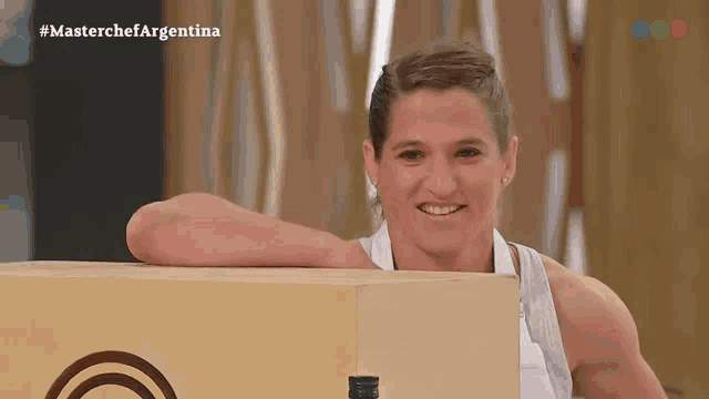 a woman leaning on a wooden box with #masterchefargentina written on the screen behind her