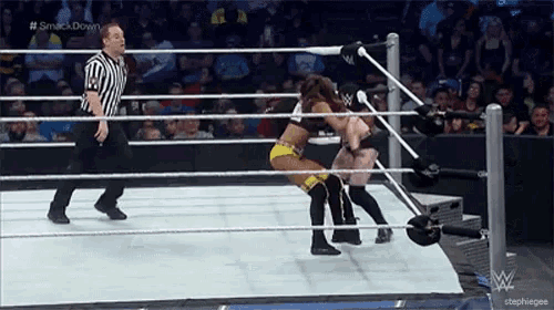 two women are wrestling in a wrestling ring while a referee stands behind them .