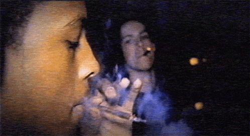 a man smoking a cigarette with a woman in the background