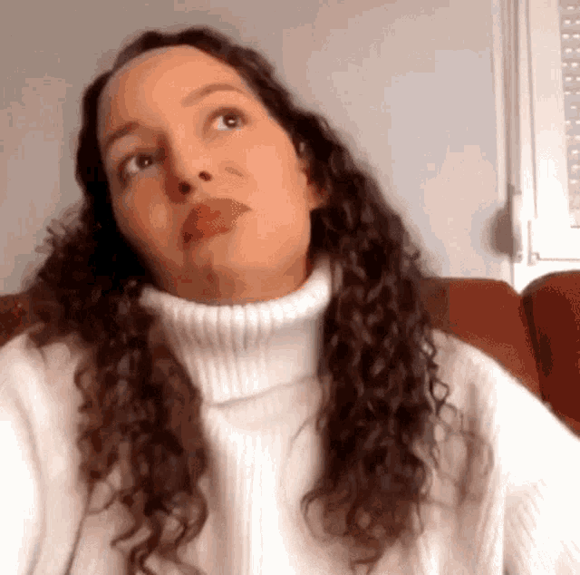 a woman with curly hair is wearing a white sweater