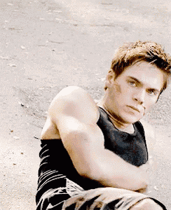 a young man in a black tank top and shorts is sitting on the ground with his arms crossed