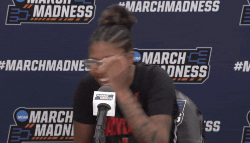 a woman smiles in front of a march madness sign