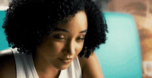 a close up of a woman 's face with curly hair and a white tank top .
