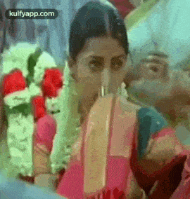 a woman is wearing a garland of flowers around her neck while a man kisses her .