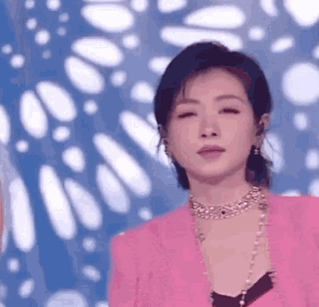 a close up of a woman wearing a pink jacket and a necklace .