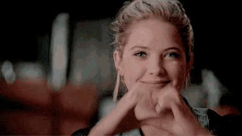 a woman is making a heart shape with her hands while smiling .