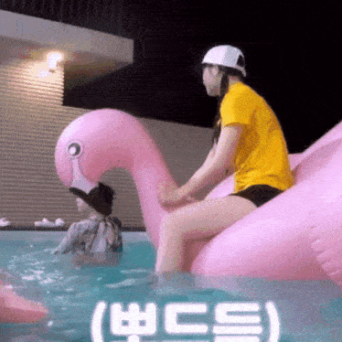 a woman in a yellow shirt sits on a pink flamingo float in a pool