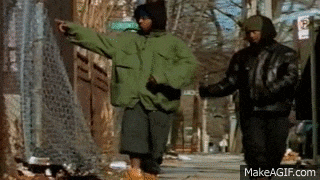 a man in a green jacket is pointing at something while walking down a sidewalk with other men .