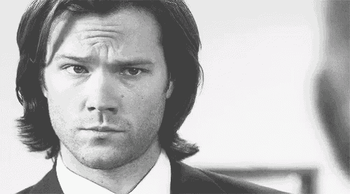 a man with long hair and a beard is wearing a suit and tie and making a funny face .