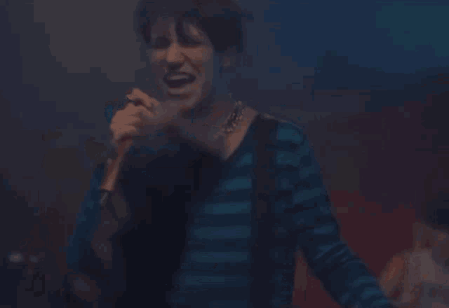 a man in a striped shirt is singing into a microphone while playing a guitar .