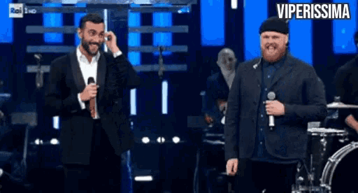 two men standing on a stage with a sign that says viperissima above them