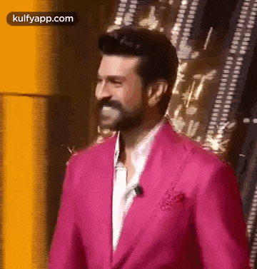 a man in a pink suit is standing in front of a yellow wall .