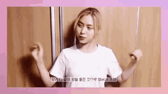 a woman in a white t-shirt is standing in front of a wall with her hands in the air .