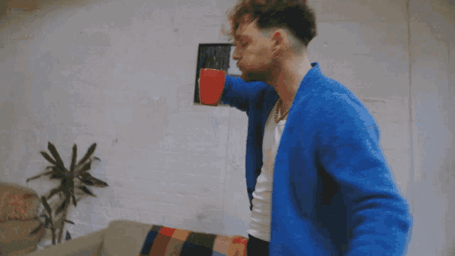 a man in a blue cardigan is holding a red cup with his arms outstretched