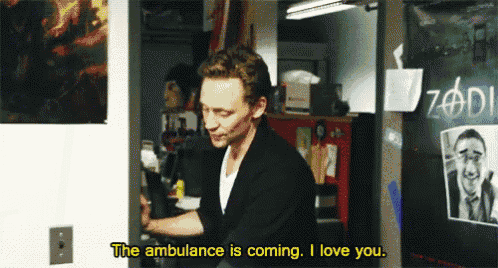 a man is sitting in a room with a sign that says the ambulance is coming i love you .