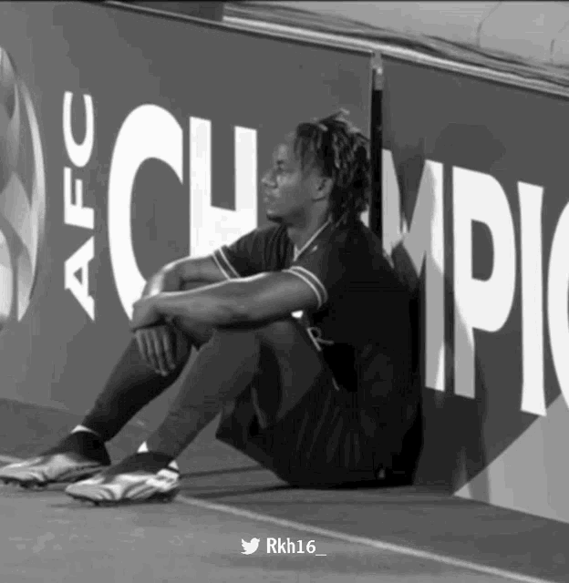 a black and white photo of a soccer player sitting in front of an afc banner