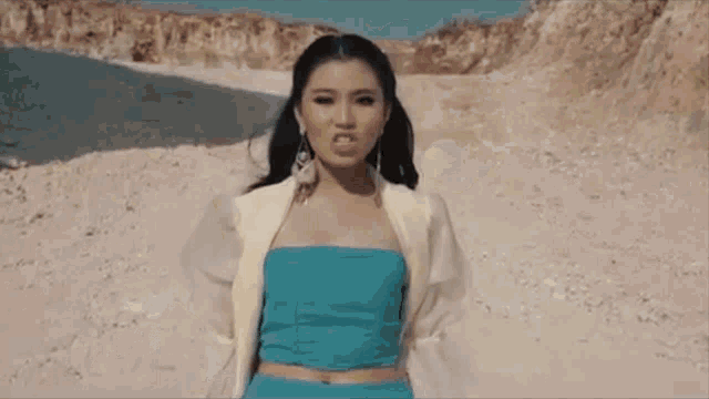 a woman in a blue top and white jacket is standing on a dirt road .