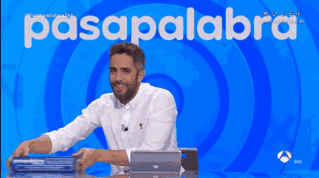 a man in a white shirt is sitting at a desk in front of a blue background that says pasapalabra