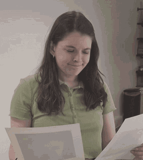 a woman in a green shirt is smiling while holding a piece of paper