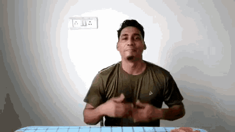 a man in a green shirt is sitting at a table with his hands on his hips .