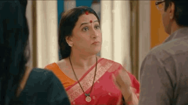 a woman in a red sari is talking to a man and a woman .