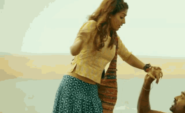 a woman is holding a man 's hand while standing next to him on the beach .