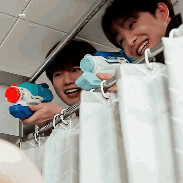 two young men are playing with water guns in a shower stall