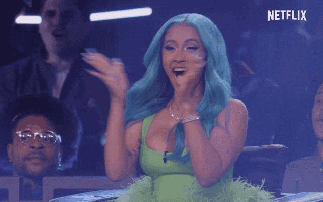 a woman with blue hair applauds in front of a netflix sign