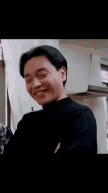 a man in a black shirt is laughing and looking down .