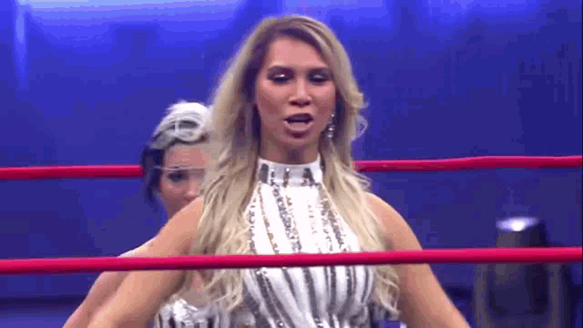 two women are standing in a wrestling ring and one is wearing a white dress .
