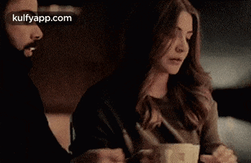 a man and a woman are sitting at a table with a cup of coffee in front of them .