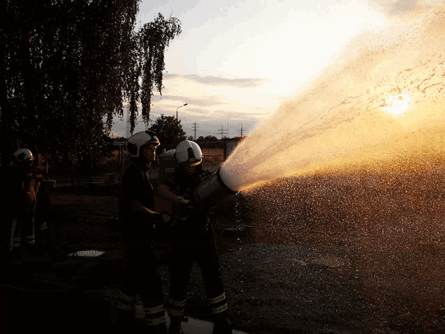 two firefighters spraying water from a hose with the sun in the background