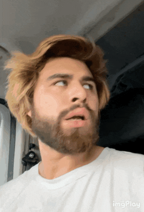 a man with a beard is wearing a white shirt and making a surprised face