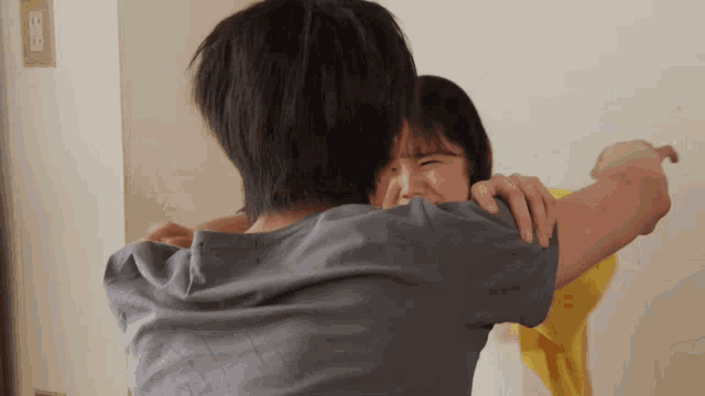 a man in a grey shirt is hugging a girl in a yellow shirt