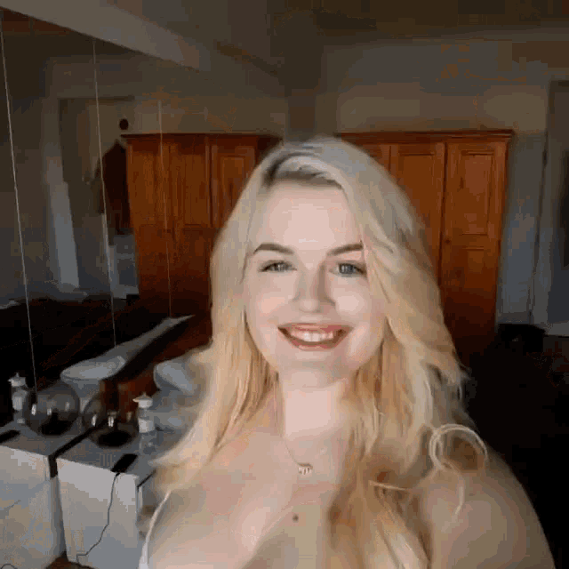 a blonde woman is smiling in front of a mirror in a room