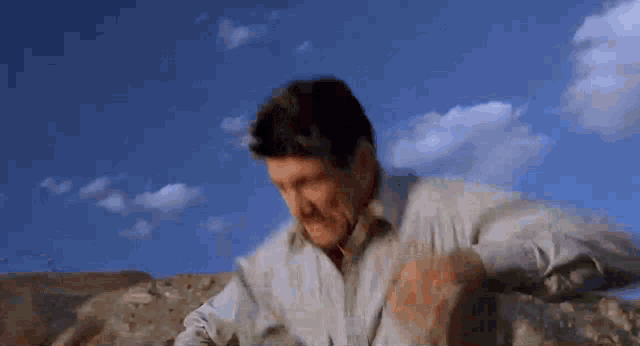 a man in a dirty shirt is standing in the desert with a blue sky in the background .