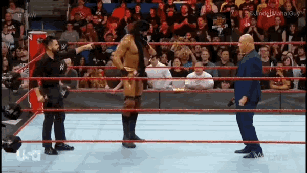 a man in a mask is standing in a wrestling ring talking to a man in a suit .