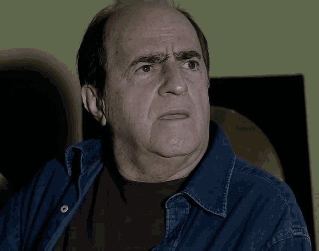 a bald man wearing a denim shirt and black shirt